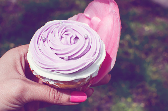 Woman holding pretty pink cupcake in hands with pink flower petals symbolic of Spring cupcakes and dessert