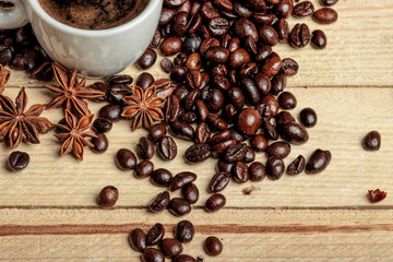 A white coffee cup on a wooden table, surrounded by coffee beans, sugar cubes, cinnamon sticks and anise flowers