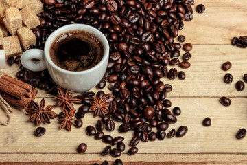 A white coffee cup on a wooden table, surrounded by coffee beans, sugar cubes, cinnamon sticks and anise flowers