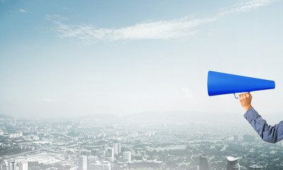 Hand of woman holding blue paper trumpet against cityscape background