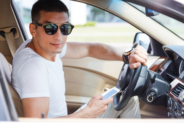 Naklejka premium Confident young rich man setting his smart phone and looking at camera while sitting in the car.