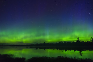 Northern lights glowing green in waves and bursts above horizon of night wilderness