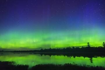 Vibrant green northern lights glowing on horizon and reflecting in lake