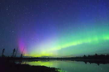 Aurora Borealis glowing green in night sky full of stars, pink colour bursting up