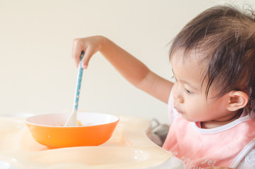 Asian toddler girl eating cereals with milk on high chair at home