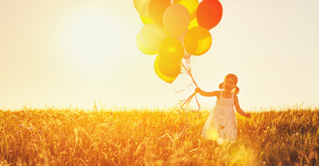 Happy cheerful child girl with balloons on meadow at sunset in summer