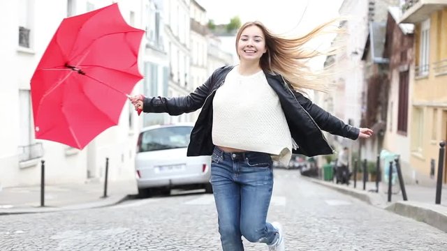 slow motion of beautiful happy smiling woman dancing and turning around with red umbrella outside on the street
