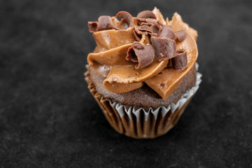 Chocolate cupcake garnished with chocolate scraps and chocolate frosting on black background