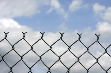 Chain link fence against blue sky and clouds 