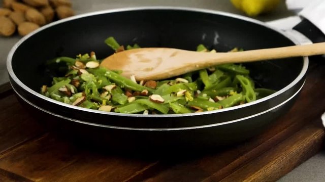 Green beans with roasted almonds on fry pan on kitchen countertop. Rotating slide.