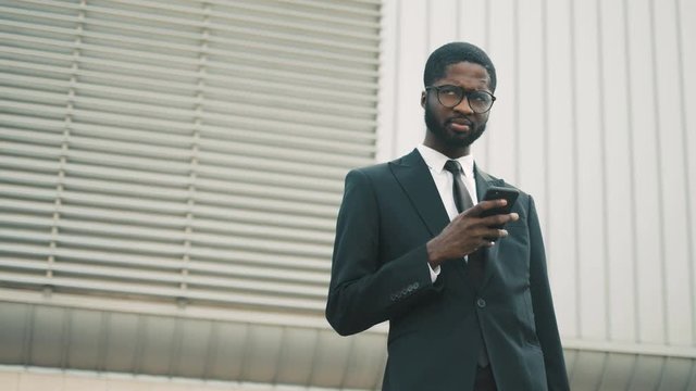 Young black african american buisnessman using smart phone outdoors near office center building. Business man reading news, checking information, surfing internet on mobile phone