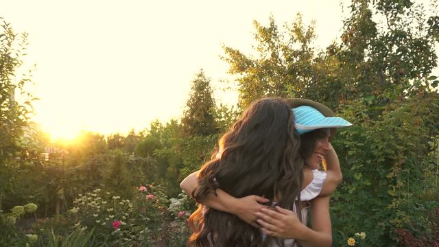 Two young attractive sisters in white dresses. Girls are fooled with hats, dancing and hugging. Family time. The joy of family communication.