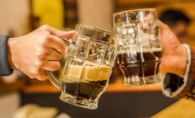 Happy male friends clinking with beer mugs in pub