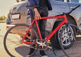 A man holds single speed bicycle near the car.