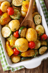 Vegan food: potatoes baked with zucchini, pepper and tomatoes close-up in baking dish. vertical top view