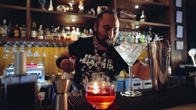 Charismatic bartender with piercings and dreadlocks making cocktail