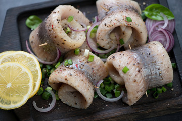 Herring fillet rolls served with green and red onion, lemon and spices. Closeup, selective focus
