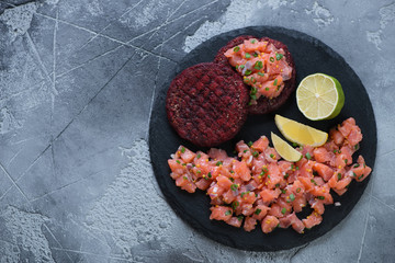 Stone slate with salmon tartar and beetroot cutlets. Flat-lay on a grey stone background with copyspace, horizontal shot