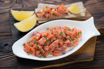 Glass plate with salmon tartar on a rustic wooden serving board, close-up, selective focus