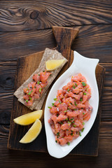 Above view of a glass plate with salmon tartare on a rustic wooden background, studio shot