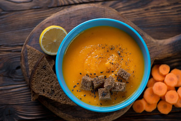 Bowl of carrot cream-soup with croutons on a rustic wooden background, view from above