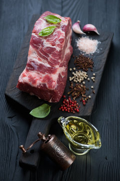 Black wooden serving board with fresh uncooked pork neck part and condiments, vertical shot, selective focus