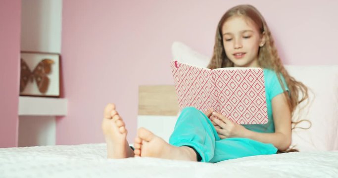 Happy student reading book on the bed. Girl something writing and laughing