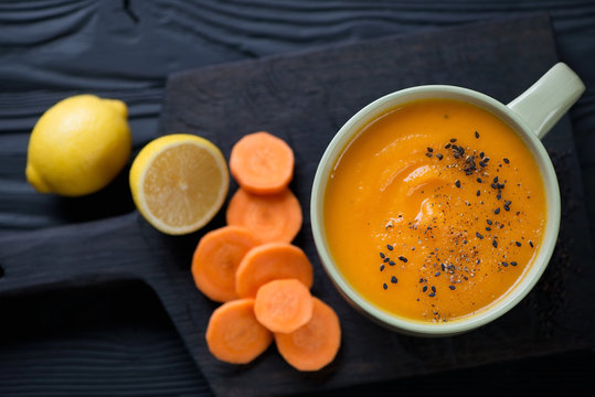Bowl with carrot cream-soup over black wooden background, above view, horizontal shot