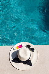 Fototapeta na wymiar Hat, sunglasses and sunscreen at the side of swimming pool, summer travel concept