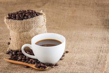Coffee beans in a sack and fresh coffee in a cup over cloth texture and background