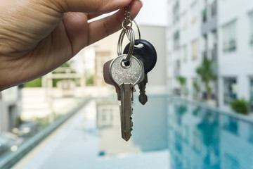 A hand is holding a key from the new condominium High rise condominium buildings and swimming pool background.