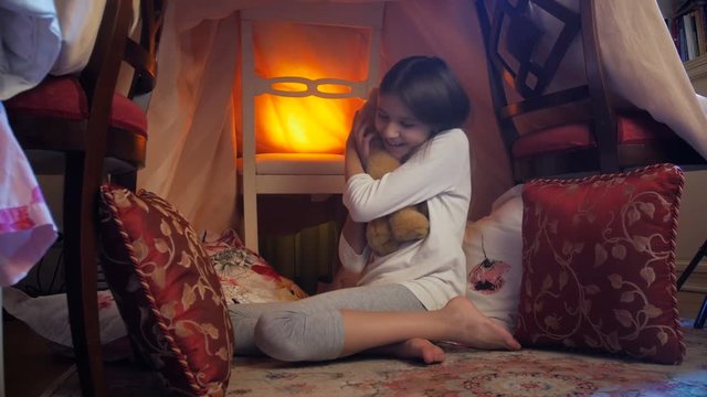 4k video of cute girl sitting in tent at bedroom and hugging big teddy bear