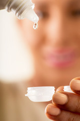 Young woman holding contact lenses cases and lens in front of her face