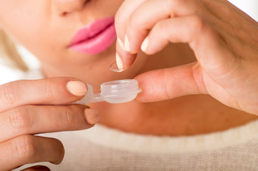 Young woman holding contact lenses cases and lens in front of her face