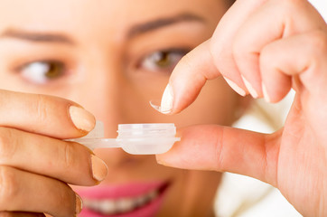 Young woman holding contact lenses cases and lens in front of her face