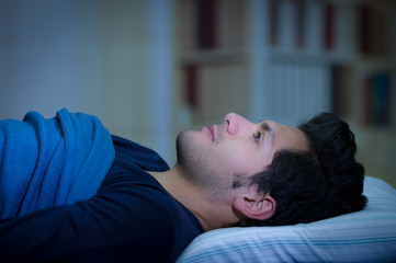 Handsome young man in bed with eyes opened suffering insomnia and sleep disorder thinking about his...