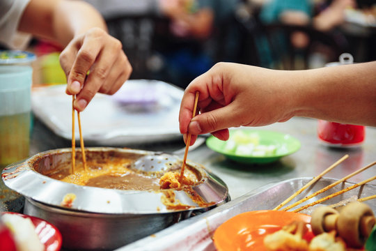 Dipping ingredients and seafood sticks in warming satay sauce. Satay is a dish of skewered grilled meat with Javanese origins in Malacca City, Malacca, Malaysia.