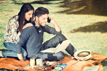 Young happy couple enjoying picnic in park while the guy use his cellphone, vintage effect