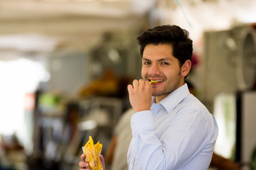 Handsome young businessman eating a delicious slices fried plantain inside of a plastic bag in a public market