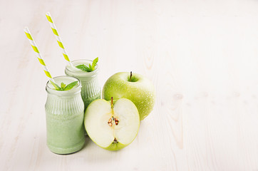 Freshly blended green apple fruit smoothie in glass jars with straw, mint leafs, apples. White wooden board background, copy space.