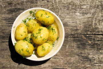 Boiled new potatoes with butter and dill on old wooden table. Top view