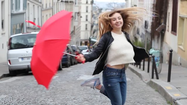 very happy, smiling and joyful girl jumping, laughing and turning on the street outside, young beautiful attractive caucasian woman having fun with red umbrella