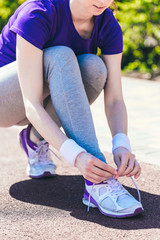 sport, fitness, people and lifestyle concept - close up of woman tying shoelaces outdoors