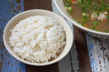 White jasmine rice bowl hot and spicy pork rib hot pot on wooden table. Main meal of thai people, a lot of carbohydrate.