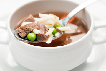 A bowl of delicious beef and barley soup with carrots, tomato, potato, celery, and peas.