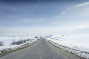 Winter sunny road to mountains at the blue skyline with a lot of snow everywhere