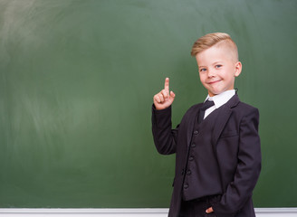 boy stands near empty chalkboard and showing finger up