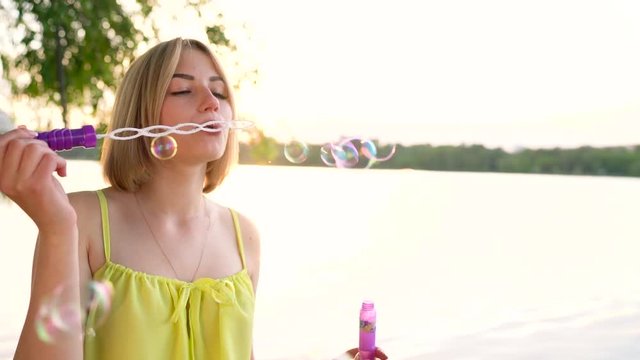 Young beautiful blonde blowing soap bubbles outdoors - slow motion