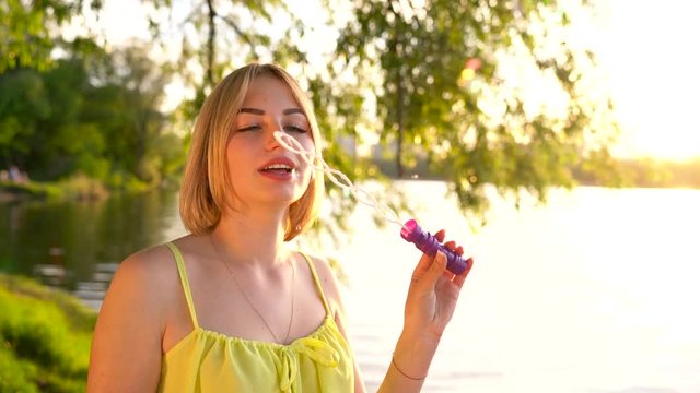 Young beautiful blonde blowing soap bubbles outdoors - slow motion