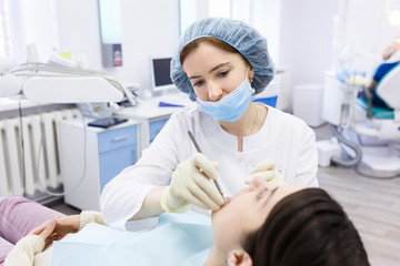 Young female patient in dentist office. Dentist examines the patient teeth at dental chair with open mouth, dental procedure in clinic